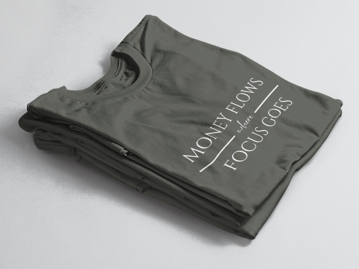 Greeb folded tee with white text “Money Flows Where Focus Goes” in elegant serif font, with horizontal lines next to “where"