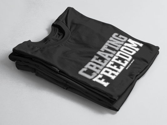 Black folded tee with bold gray and white text “Creating Freedom” and small “Brick by Brick” centered below.