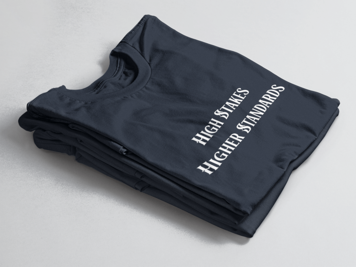 Navy folded tee with white gothic-style text reading “High Stakes Higher Standards” centered on the front.