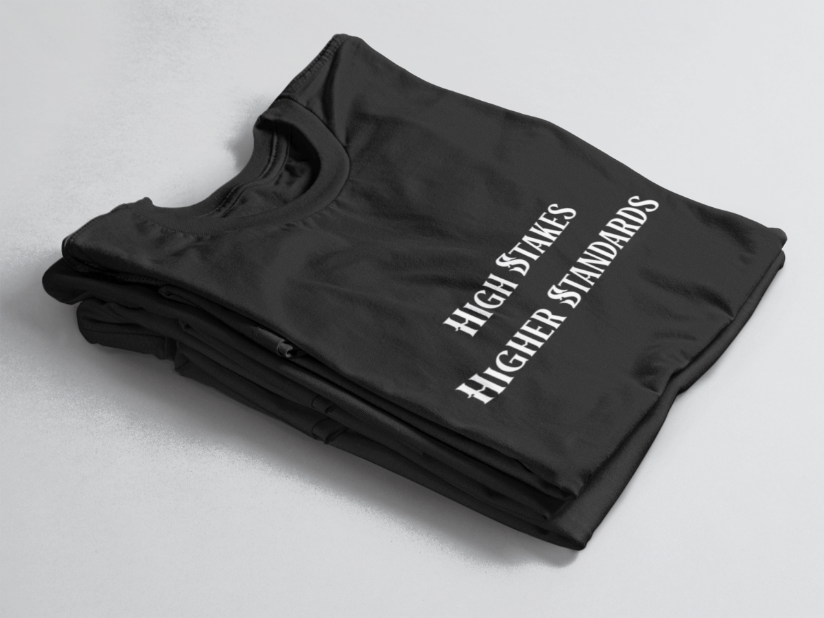 Black folded tee with white gothic-style text reading “High Stakes Higher Standards” centered on the front.