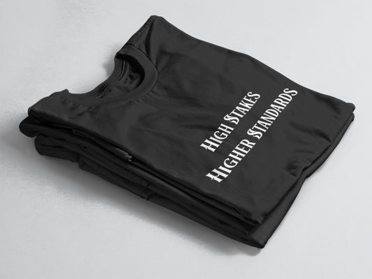 Black folded tee with white gothic-style text reading “High Stakes Higher Standards” centered on the front.