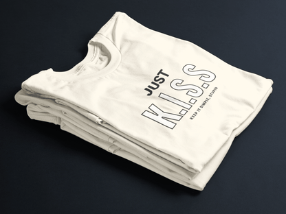 Beige folded t-shirt with bold black text “JUST K.I.S.S” and smaller text “Keep It Simple, Stupid” centered on the front.