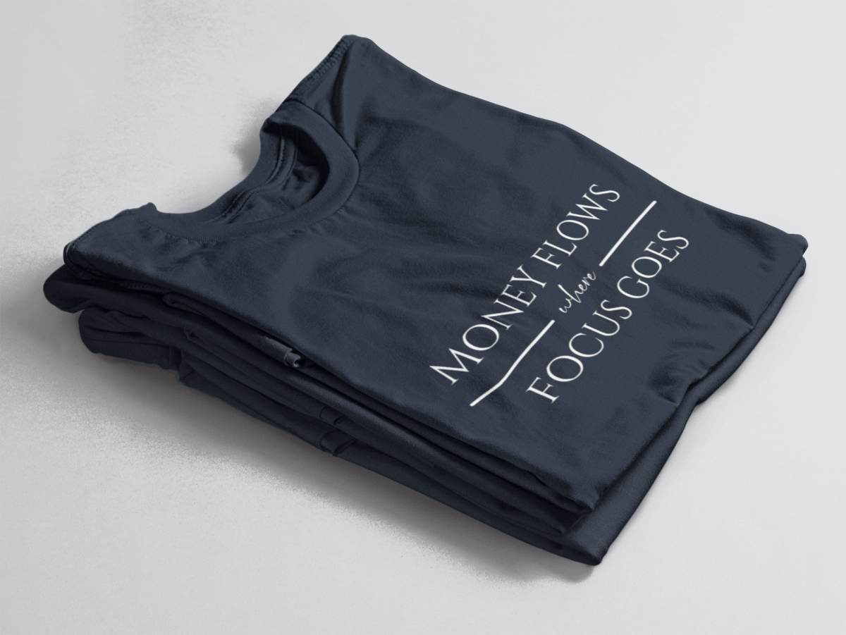 Navy folded tee with white text “Money Flows Where Focus Goes” in elegant serif font, with horizontal lines next to “where"