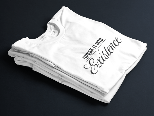 White folded tee with black text “Speak It Into” in bold caps above cursive “Existence” centered on the front.