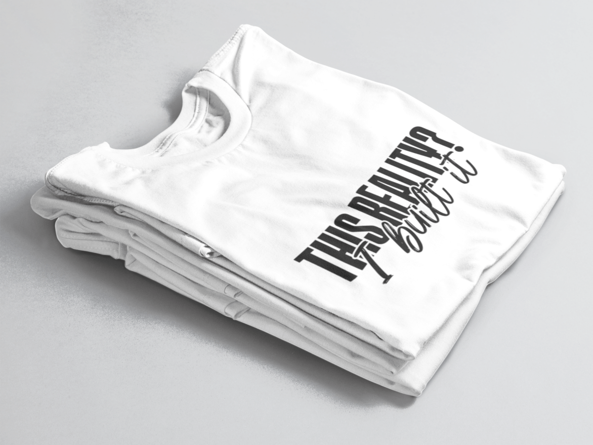 White folded tee with bold outlined text “This Reality?” above cursive “I built it” in white script.