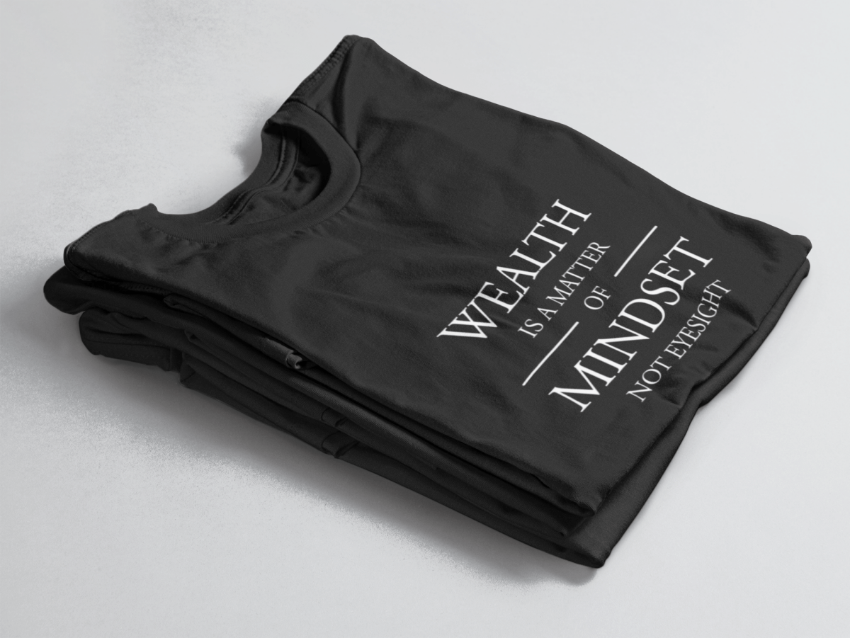 Black folded tee with white text “Wealth is a Matter of Mindset, Not Eyesight” in elegant serif font with horizontal lines.