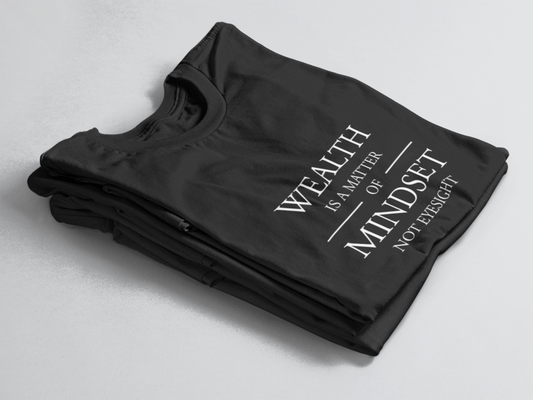 Black folded tee with white text “Wealth is a Matter of Mindset, Not Eyesight” in elegant serif font with horizontal lines.