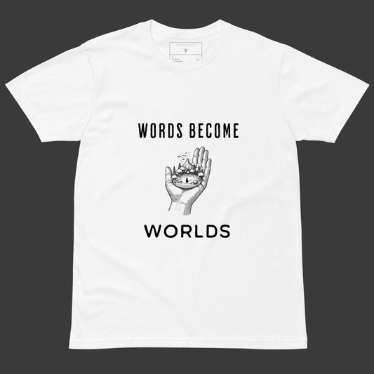 White tee with black text “Words Become Worlds” and a hand holding a tiny illustrated world in the center